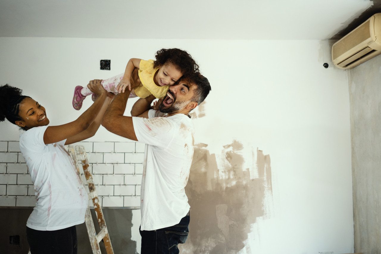 A playful, happy family renovating their home and lifting their child in the air. 