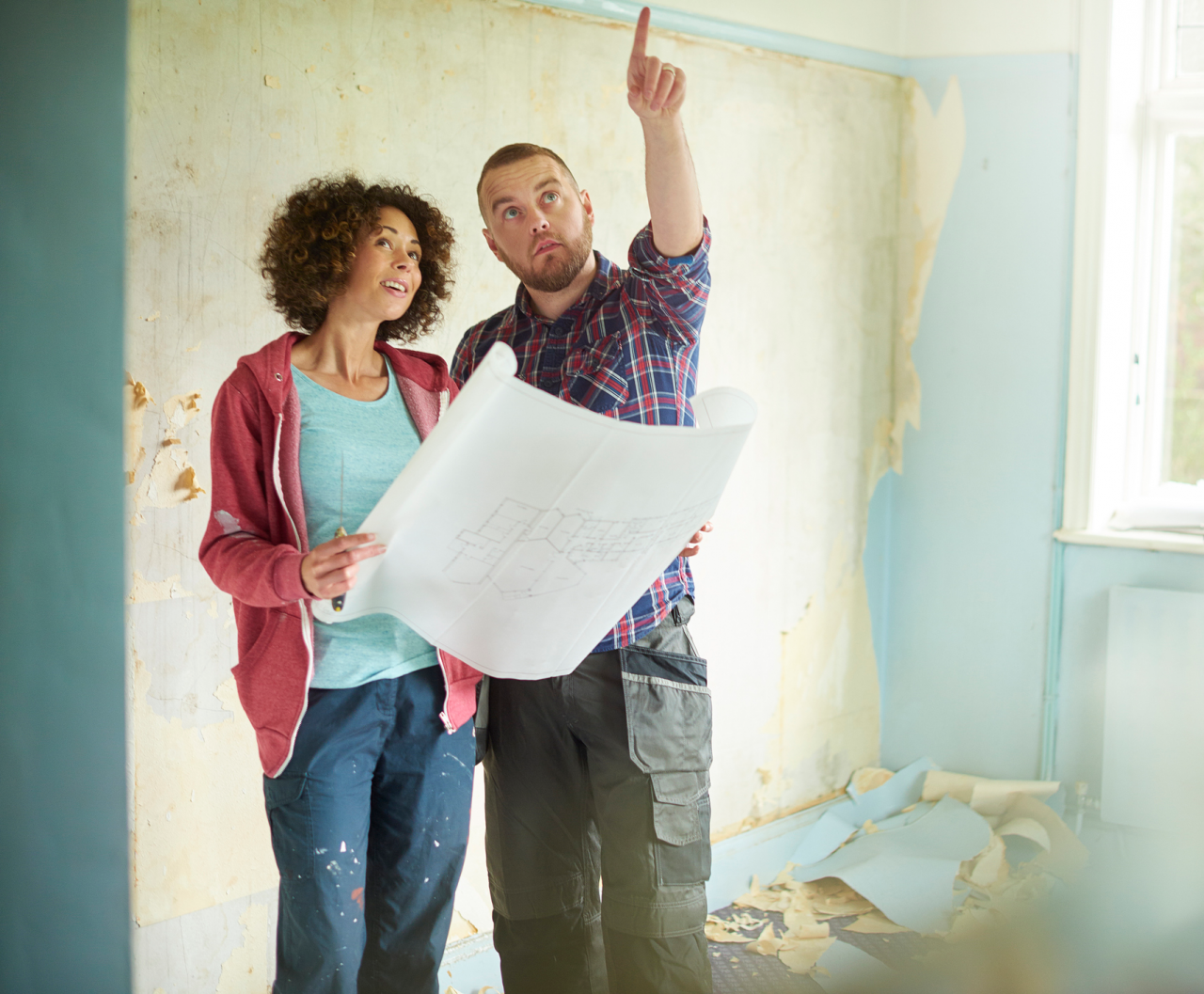 A couple looking at a blueprint discussing a renovation in their house.